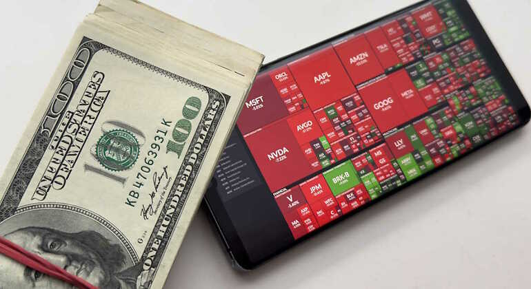 Un fajo de billetes de dólar y los resultados de la bolsa en rojo